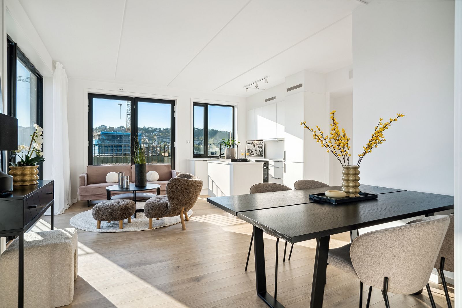 A modern living room with a sofa, coffee table, and ottomans, a dining area with a table and chairs, and large windows offering a city view.