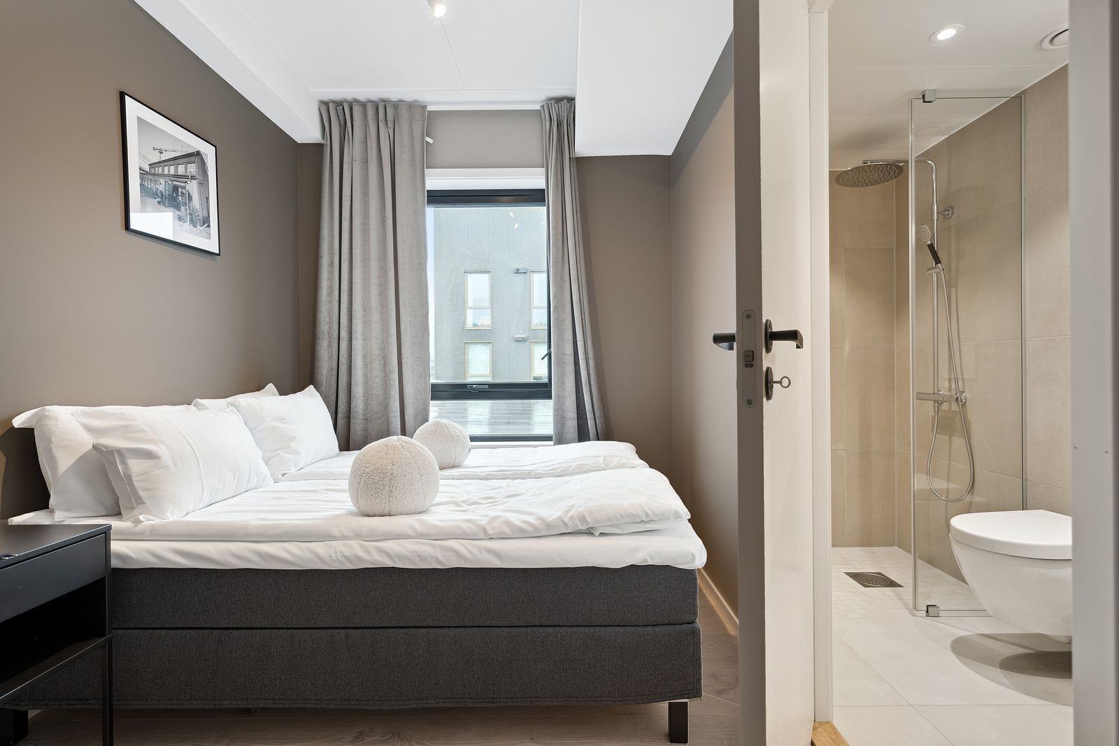 Une chambre moderne avec un grand lit, une table de chevet, un espace douche et une vue sur la ville par la fenêtre.