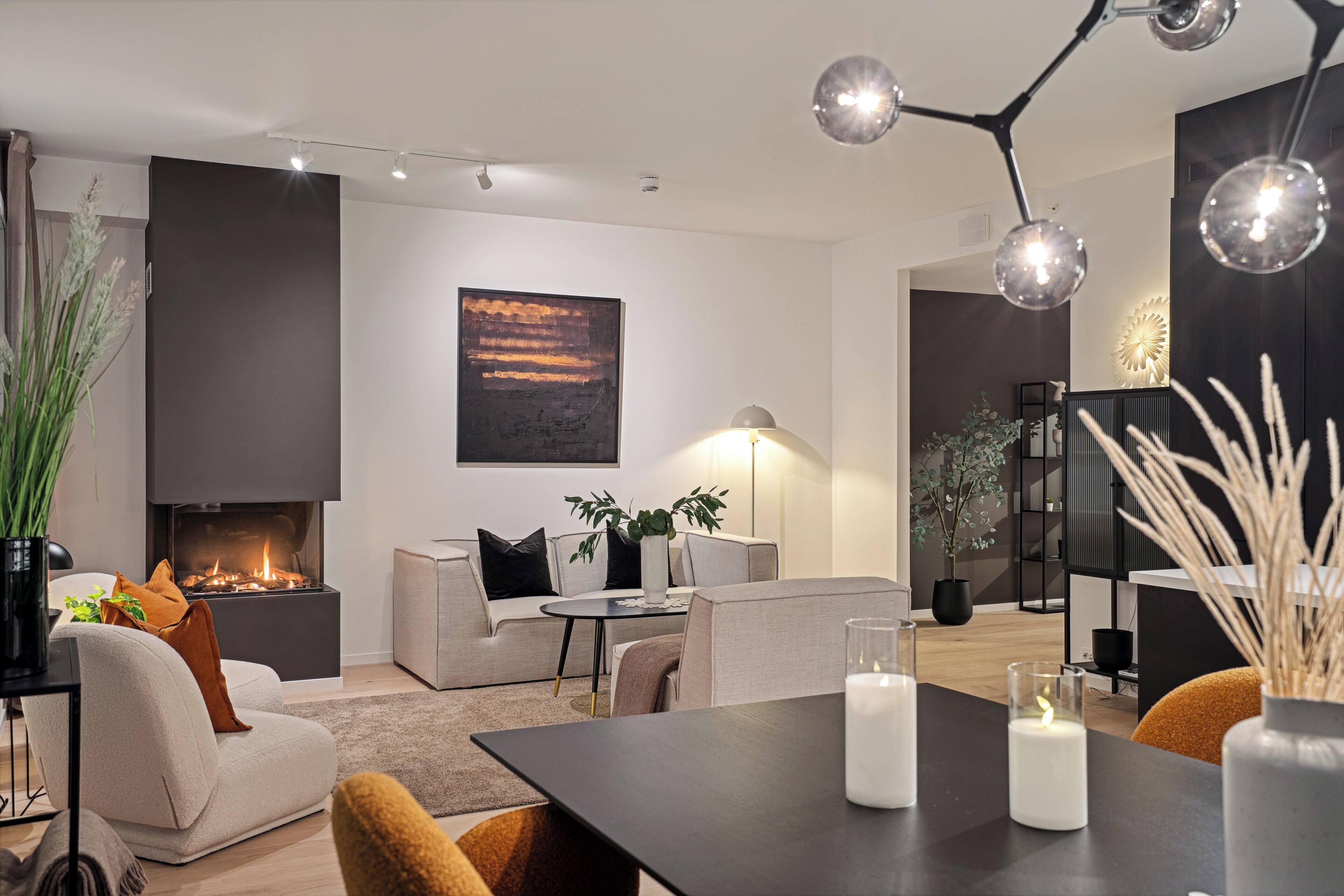Ein modernes Wohnzimmer mit Kamin, einer Couch, einem Esstisch mit Kerzen und einem großen abstrakten Gemälde an der Wand.