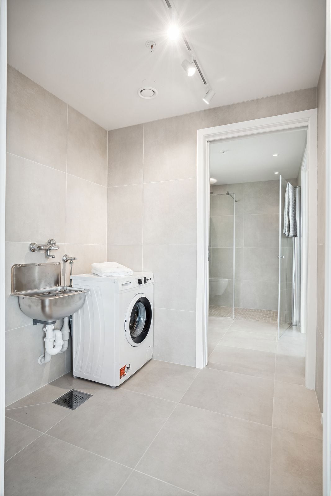 Une salle de bain moderne équipée d’un lave-linge, d’un évier et d’un espace douche.