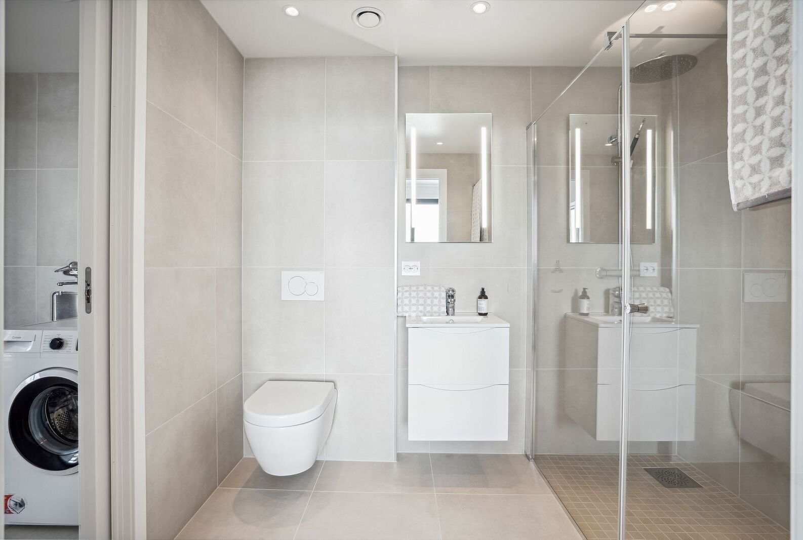 A modern bathroom with a glass-enclosed shower, a toilet, and a washing machine in the adjacent space.