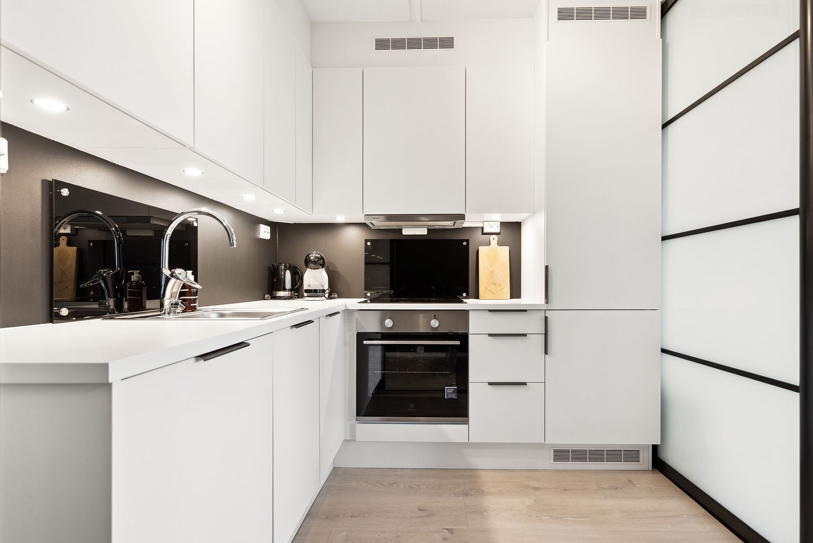 Una cucina moderna con mobili bianchi, un lavello in acciaio inossidabile e un forno integrato.