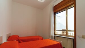 Quarto com duas camas, janela com vista para uma varanda e radiador.