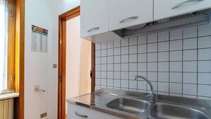 Cozinha com armários brancos, pia de aço inoxidável e painel de azulejos.