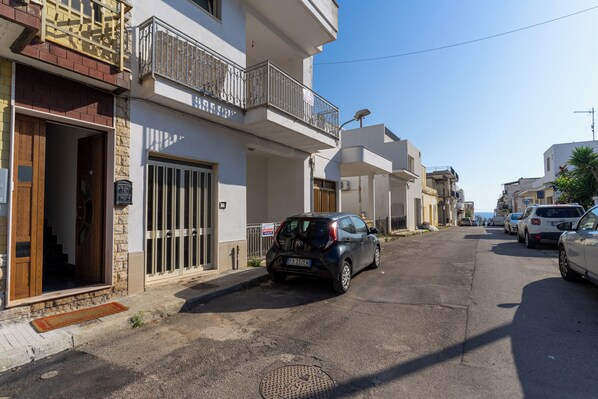 Rua residencial com casas, um carro estacionado e céu claro.