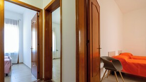 Quarto com uma cama, uma cadeira e uma porta que dá para outro cômodo.