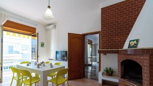 Uma sala de jantar com mesa branca e cadeiras amarelas, lareira de tijolos e varanda com vista.