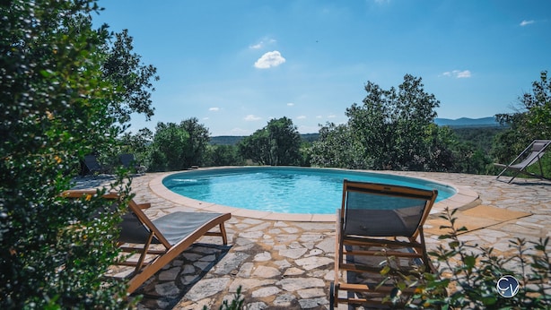A pool with lounge chairs, surrounded by stone tiles and greenery, with a view of distant hills. - Maison La Hulotte (Lussan)