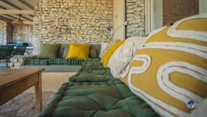 A cozy seating area with a stone wall, a sofa with green and yellow cushions, and a wooden table. - Maison La Hulotte (Lussan)