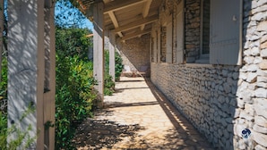A stone pathway leading to a covered outdoor seating area with a stone wall on one side and a wooden pergola on the other. - Maison La Hulotte (Lussan)