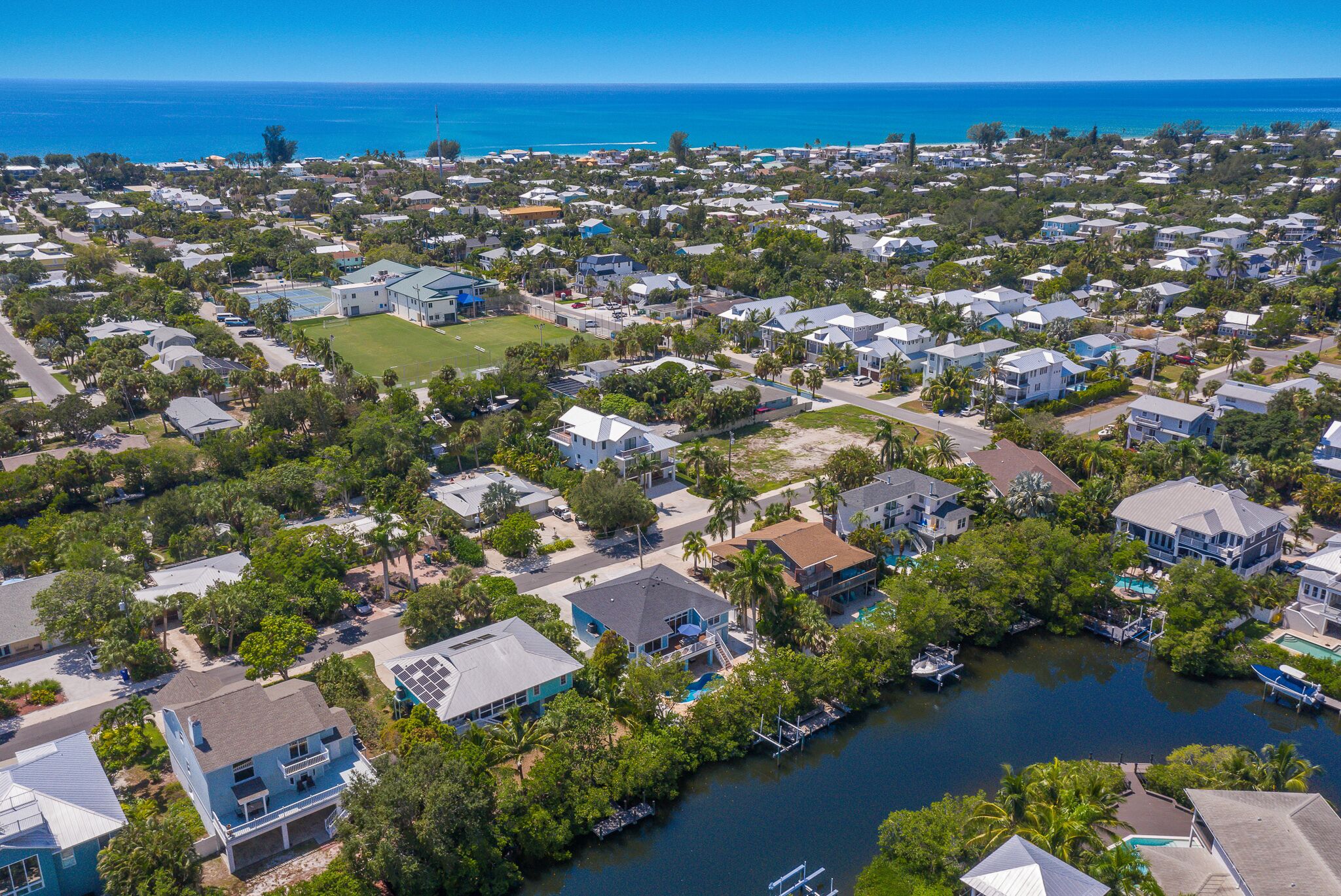 An aerial view of a residential area with houses, a marina, and a clear view of the ocean.