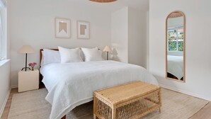 A bedroom with a bed, bedside lamps, a mirror, and a wicker bench.