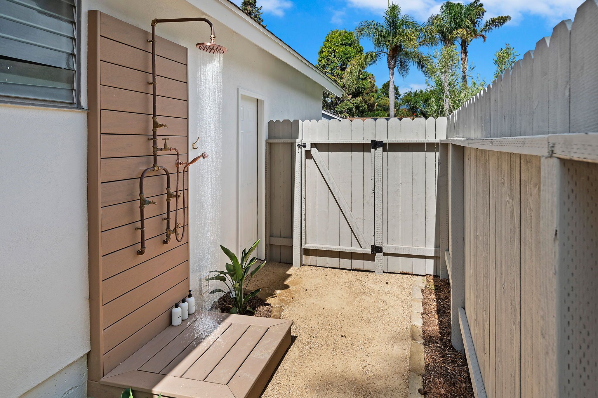 A small backyard with a wooden deck, a white fence, and a water feature.