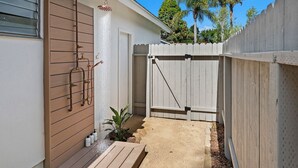 A small backyard with a wooden deck, a white fence, and a water feature.