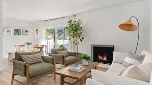A modern living room with a fireplace, two sofas, a coffee table, and a dining area with a table and chairs.