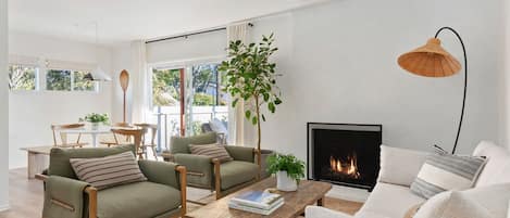 A modern living room with a fireplace, two sofas, a coffee table, and a dining area with a table and chairs.