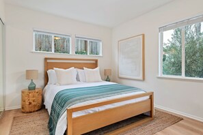 Une chambre à coucher avec un lit en bois, deux tables de chevet, une fenêtre avec des stores et un tableau encadré au mur.