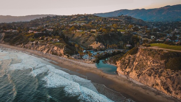 A coastal town with a beach, a river, and hills in the background.