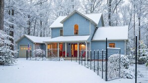 Una casa a due piani con veranda e garage, circondata da alberi innevati.