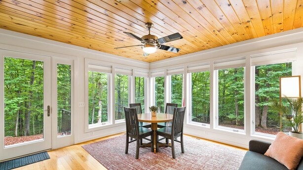 Una stanza con soffitto in legno, ampie finestre, un tavolo da pranzo con sedie e un divano.