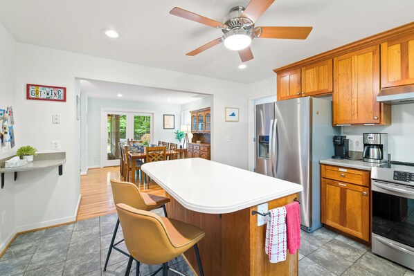 A modern kitchen with wooden cabinets, a stainless steel refrigerator, and a central island with bar stools. - 4BR/2.5BA on 5 acres near Bold Rock Cidery & Devils Backbone (Nellysford)