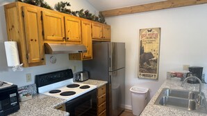 A kitchen with wooden cabinets, a stove, a refrigerator, granite countertops, a trash can, and a poster of Rocky Mountain National Park. - Lazy R Cottages: 7a 2 Bedroom Cabin (Estes Park)