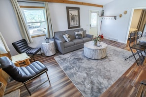 A living room with a grey sofa, black leather chairs, a round coffee table, and a grey rug. - Lazy R Cottages: 7a 2 Bedroom Cabin (Estes Park)