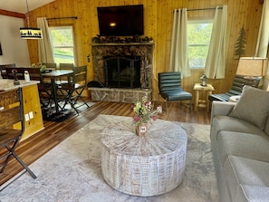 A cozy living room with a stone fireplace, wooden walls, a round coffee table, and a comfortable seating area. - Lazy R Cottages: 7a 2 Bedroom Cabin (Estes Park)