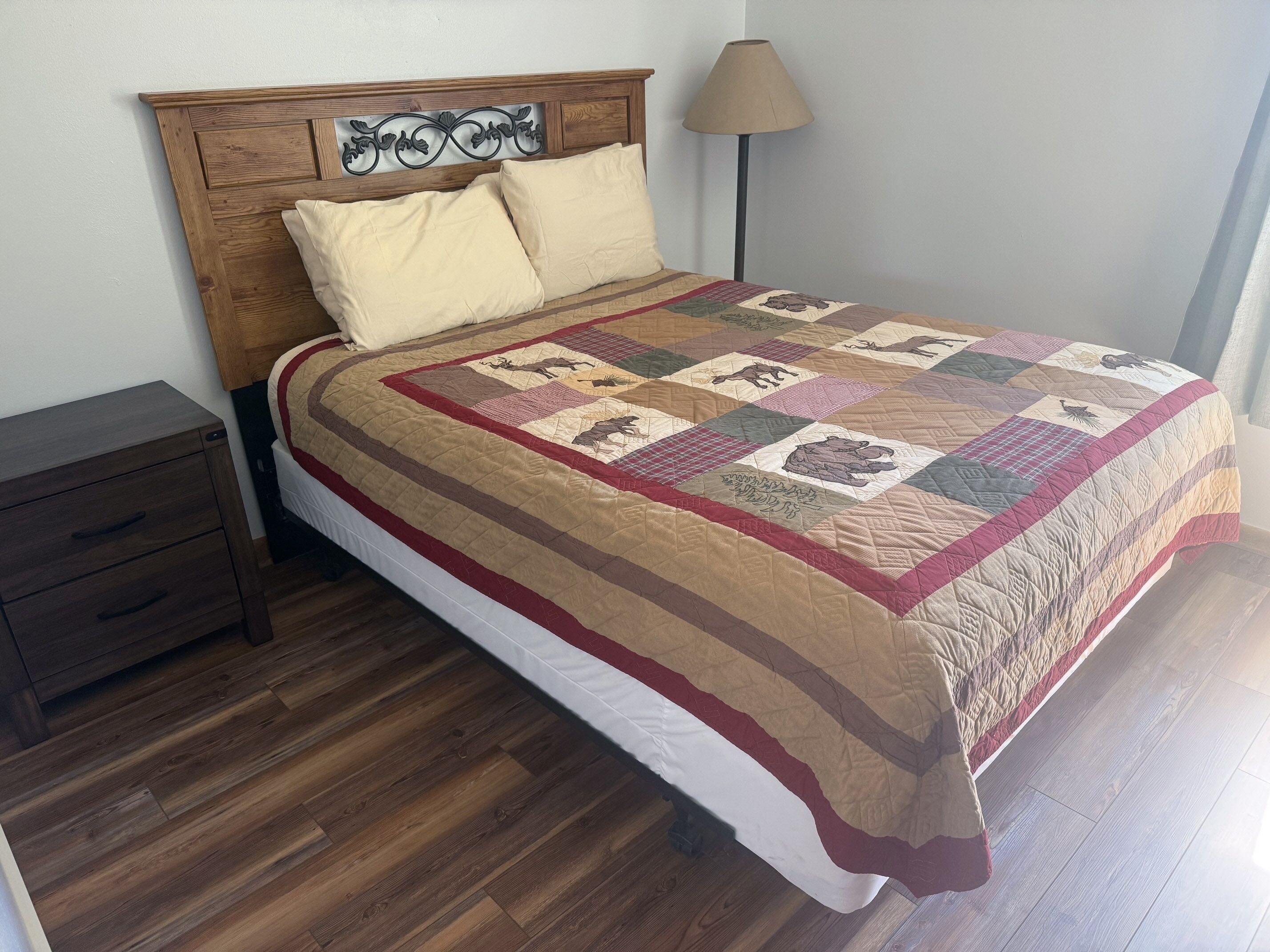 A bed with a quilt, a wooden headboard, a bedside table, and a lamp.