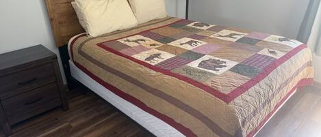 A bed with a quilt, a wooden headboard, a bedside table, and a lamp.