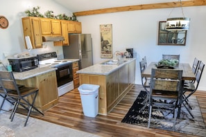 A kitchen with wooden cabinets, a stainless steel refrigerator, a granite countertop, and a dining area with a wooden table and chairs. - Lazy R Cottages: 7a 2 Bedroom Cabin (Estes Park)
