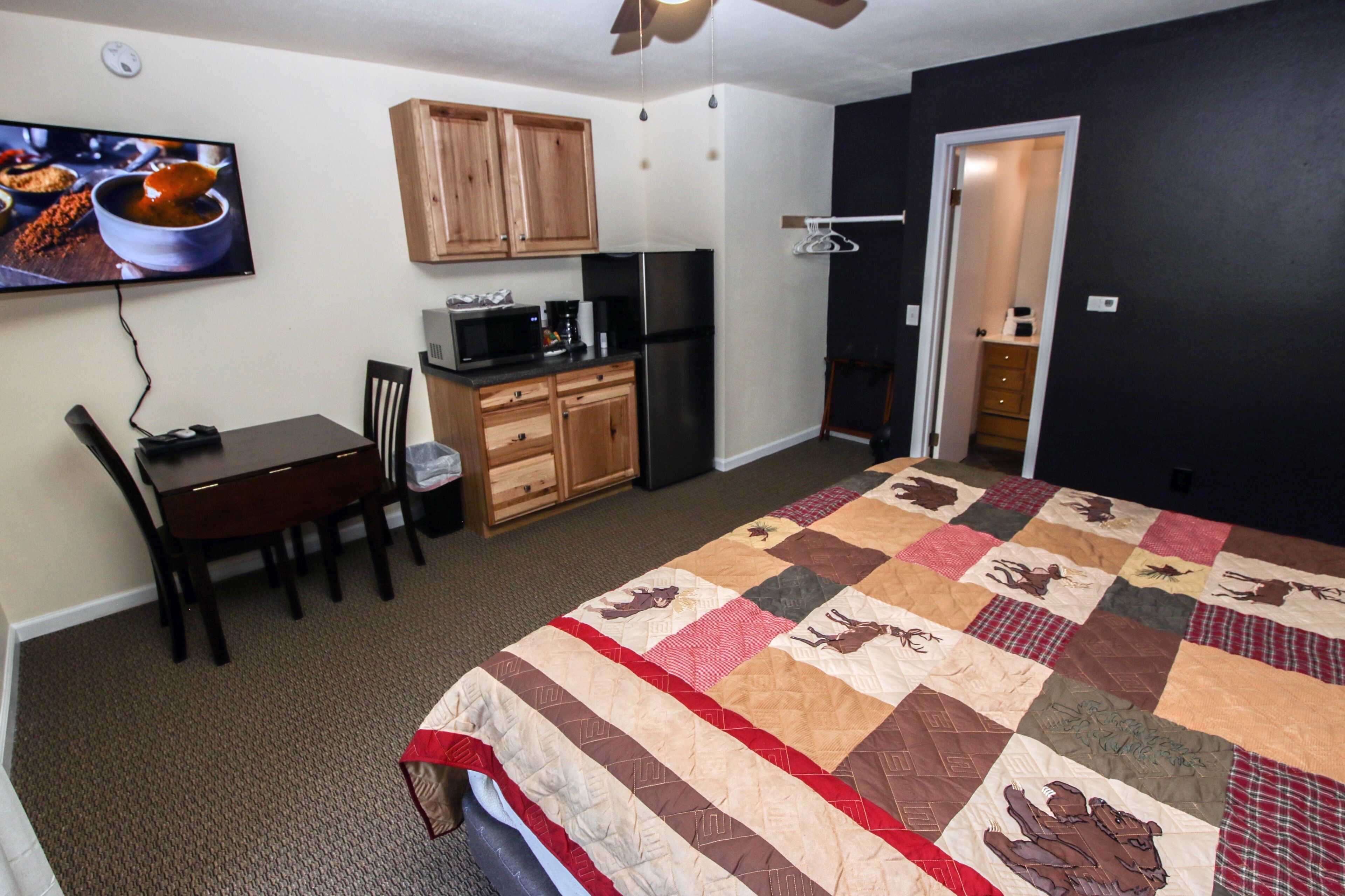 A compact room with a bed, a desk, a chair, a microwave, a refrigerator, and a television mounted on the wall.