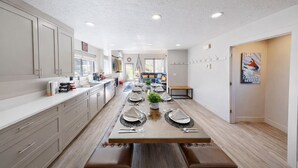 Eine moderne Küche mit einem langen Esstisch, gedeckt für sechs Personen, einem eingebauten Backofen und einem großen Fenster, das natürliches Licht hereinlässt.
