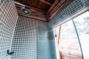 Une salle de bain avec un sol et des murs carrelés, un espace douche et une vue sur l’extérieur grâce à une porte en verre.