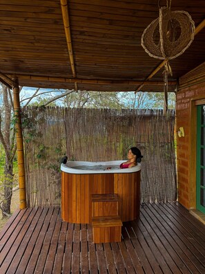 A wooden deck with a hot tub, bamboo fence, and a green door. - Bangalô Ametista (Alto Paraíso de Goiás)