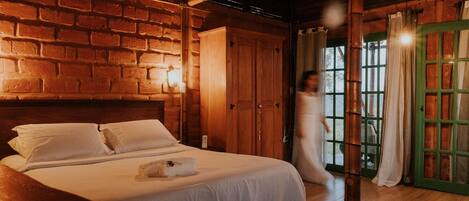A room with a brick wall, wooden ceiling beams, a bed with white linens, and a green door.
