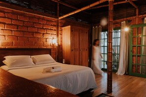 A room with a brick wall, wooden ceiling beams, a bed with white linens, and a green door. - Bangalô Ametista (Alto Paraíso de Goiás)