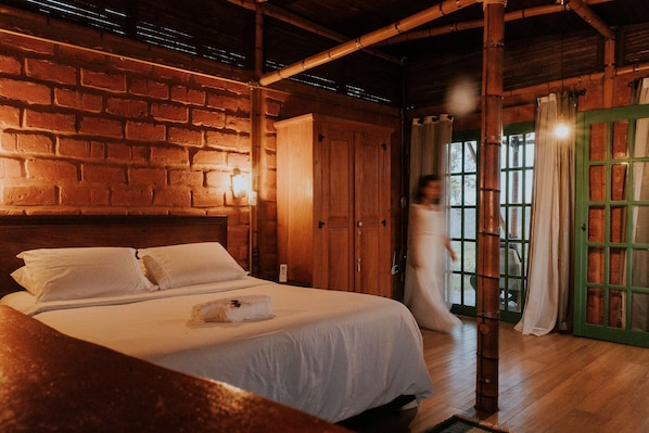 Ein Zimmer mit Backsteinwand, Holzbalkendecke, einem Bett mit weißen Leinentüchern und einer grünen Tür.