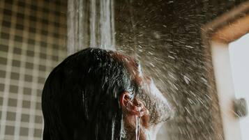 Une personne se tient sous une douche, l’eau coulant sur elle.