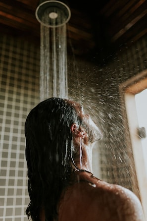 Eine Person steht unter einer Dusche, während Wasser herabrieselt.