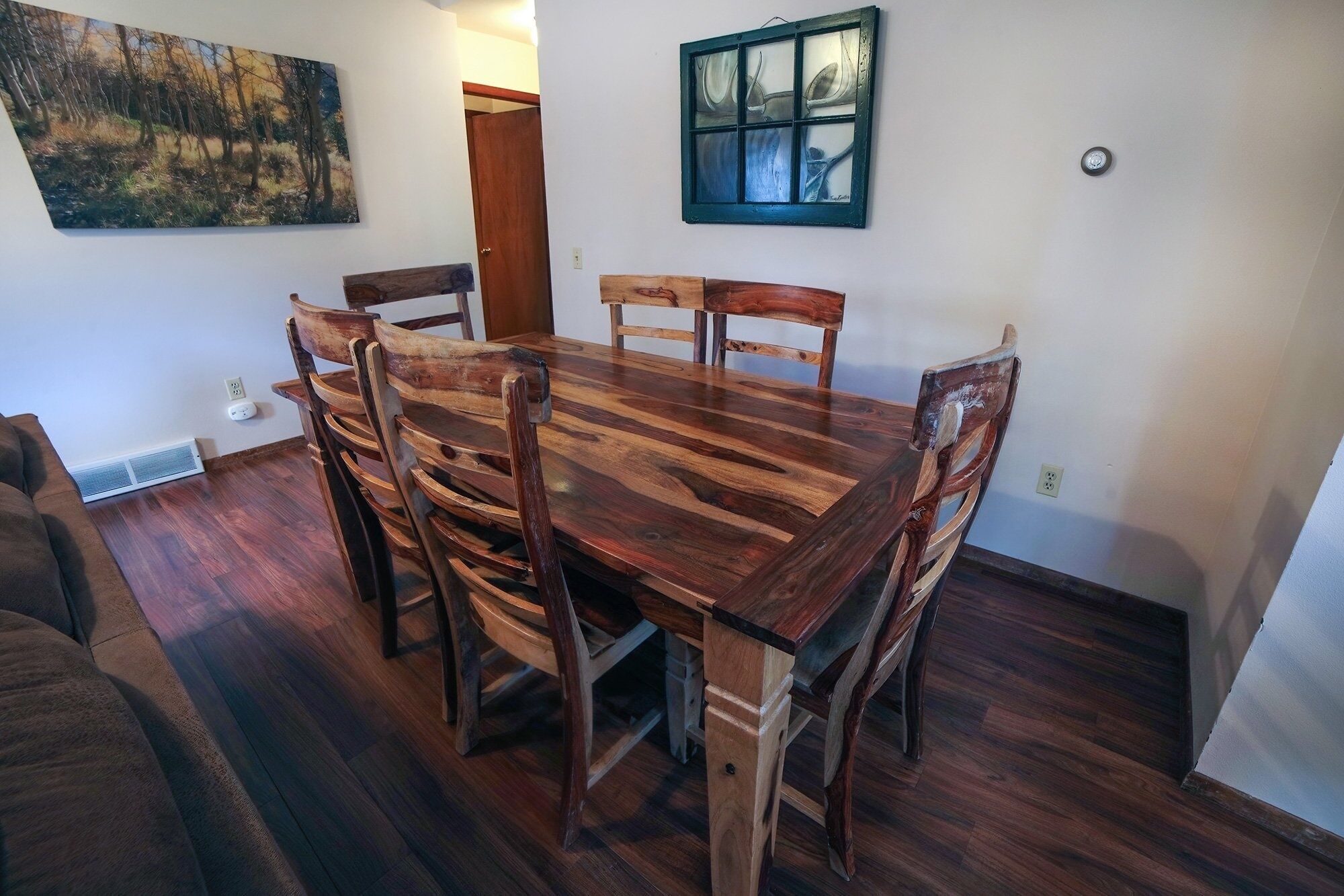 Un comedor con una mesa y sillas de madera, un cuadro en la pared y una ventana con vistas.