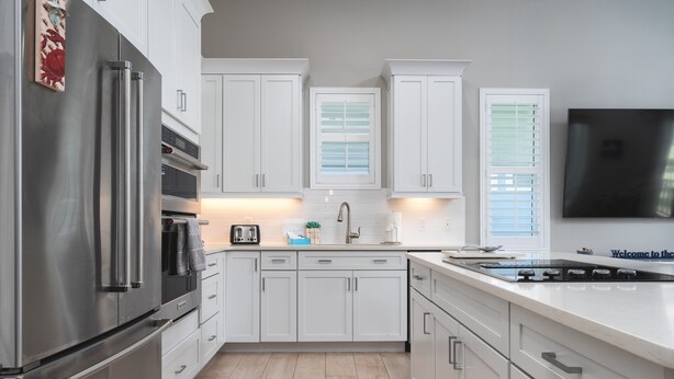 A modern kitchen with white cabinets, stainless steel appliances, and a built-in oven. - 134 Pearl St 3 Bedroom Home by RedAwning (Fort Myers Beach)