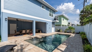 A residential backyard with a swimming pool, a covered patio area, and a brick patio. - 134 Pearl St 3 Bedroom Home by RedAwning (Fort Myers Beach)