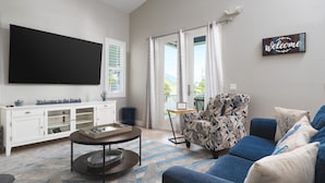 A living room with a flat-screen TV, a patterned armchair, a blue sofa, and a 'Welcome' sign. - 134 Pearl St 3 Bedroom Home by RedAwning (Fort Myers Beach)