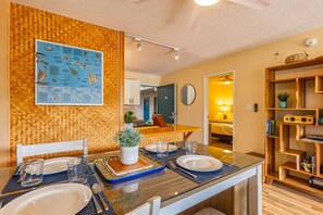 A dining area with a wooden herringbone wall, a map, and a dining table set with plates, glasses, and a plant. - Pacific Shores B113 2 Bedroom Condo (Kihei)
