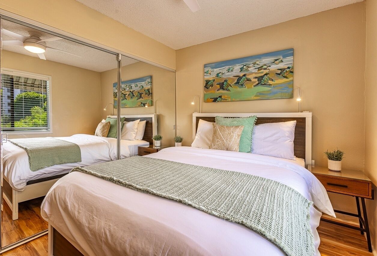 A bedroom with two beds, a large mirror, and artwork on the wall.