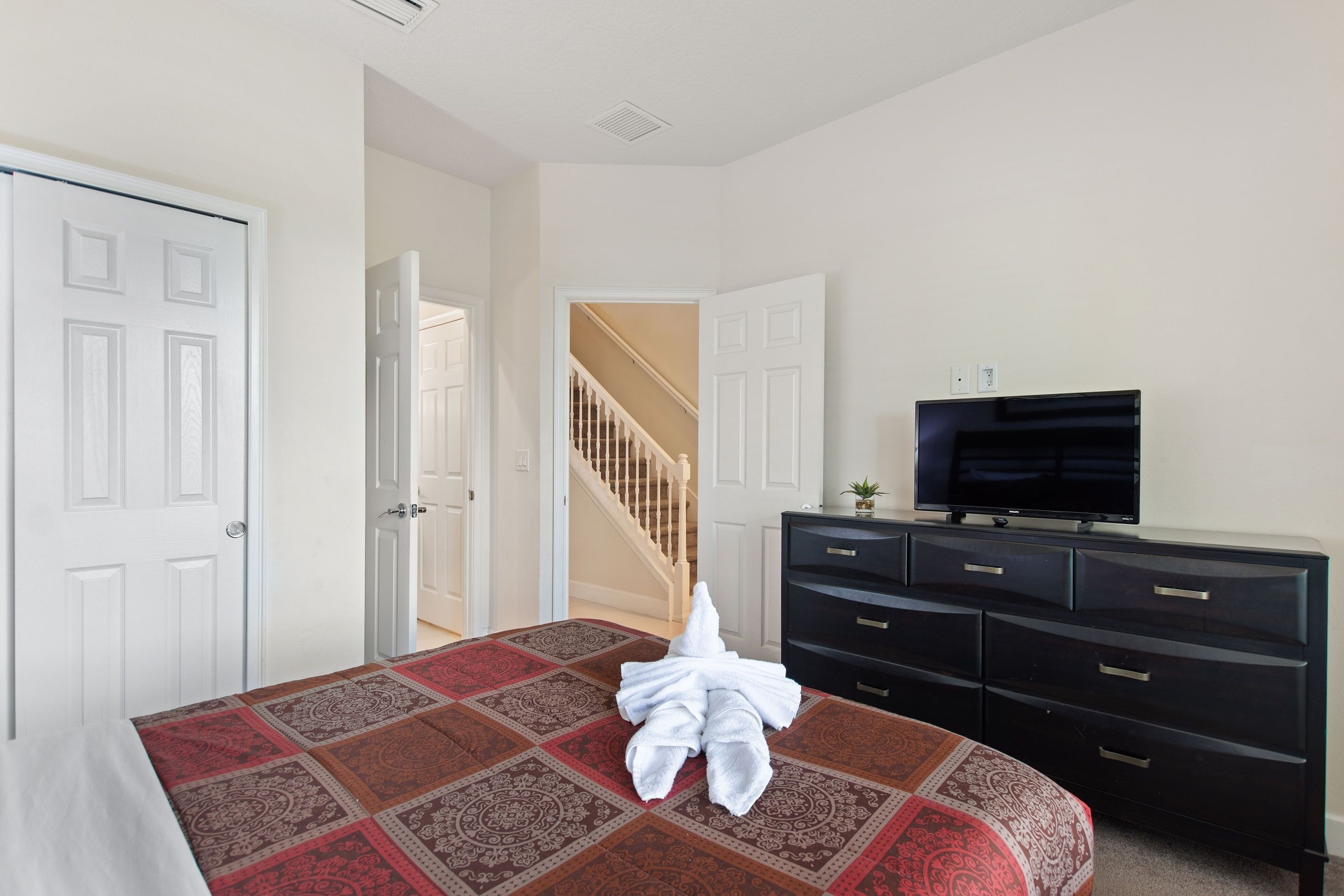 A bedroom with a bed, a TV, a dresser, and a staircase.