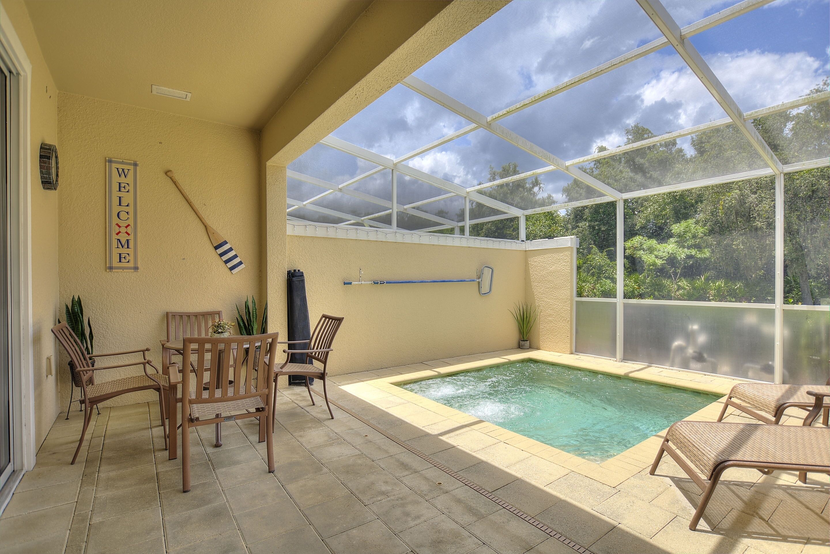 A pool area with a glass enclosure, outdoor furniture, and a 'WELCOME' sign.