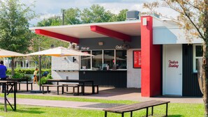 Een terras met tafels en parasols, een gebouw met een rood-witte gevel en een bordje dat binnenruimte aangeeft.