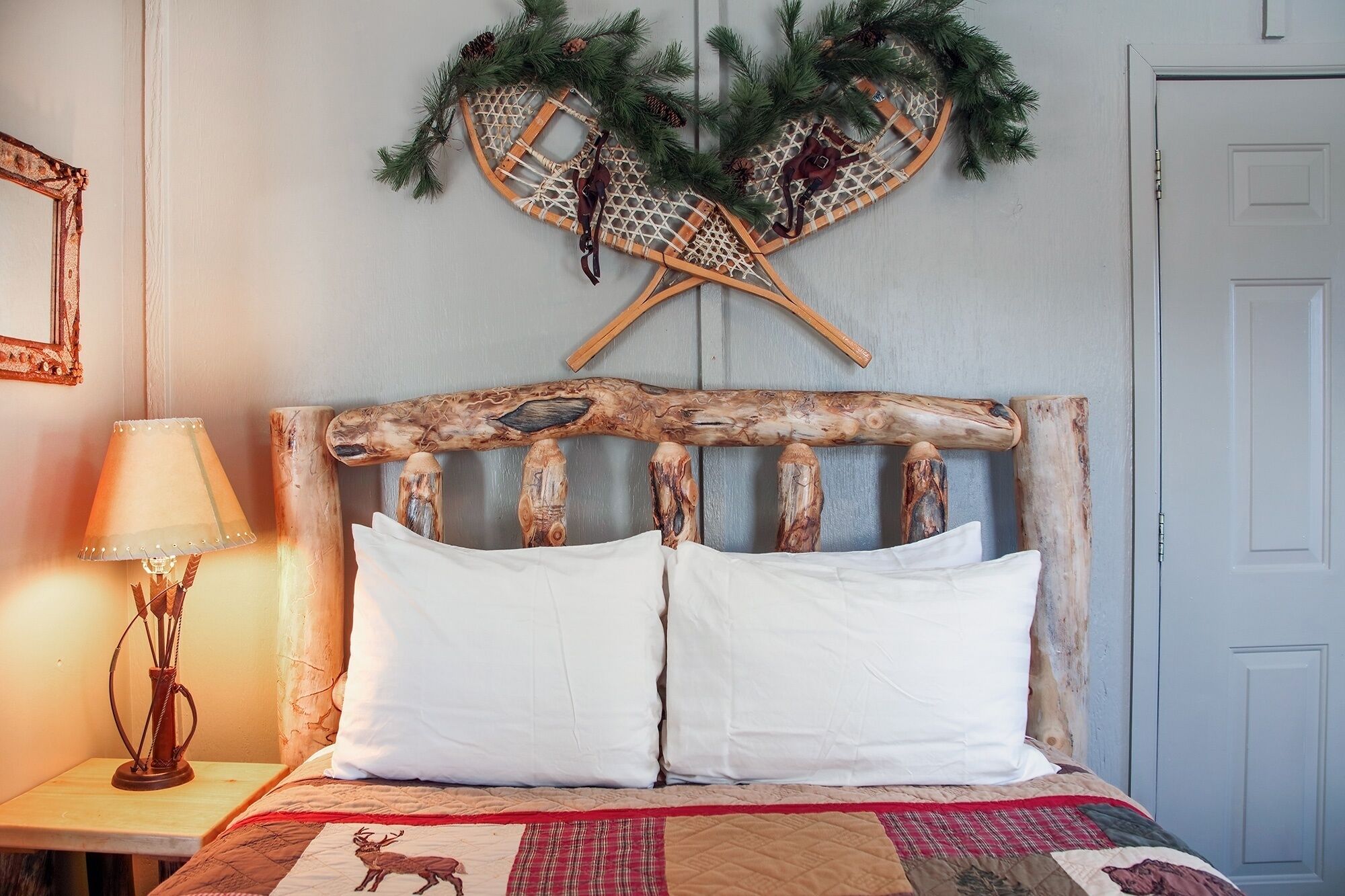 A bed with a rustic wooden headboard, white pillows, and a quilt with a deer print.